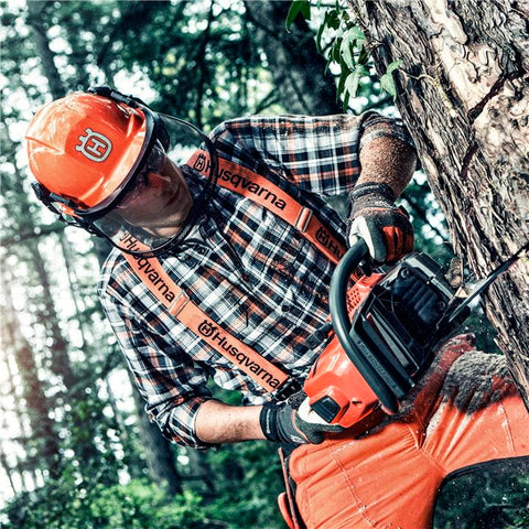 Man in the woods using chainsaw to cut down a large tree width=
